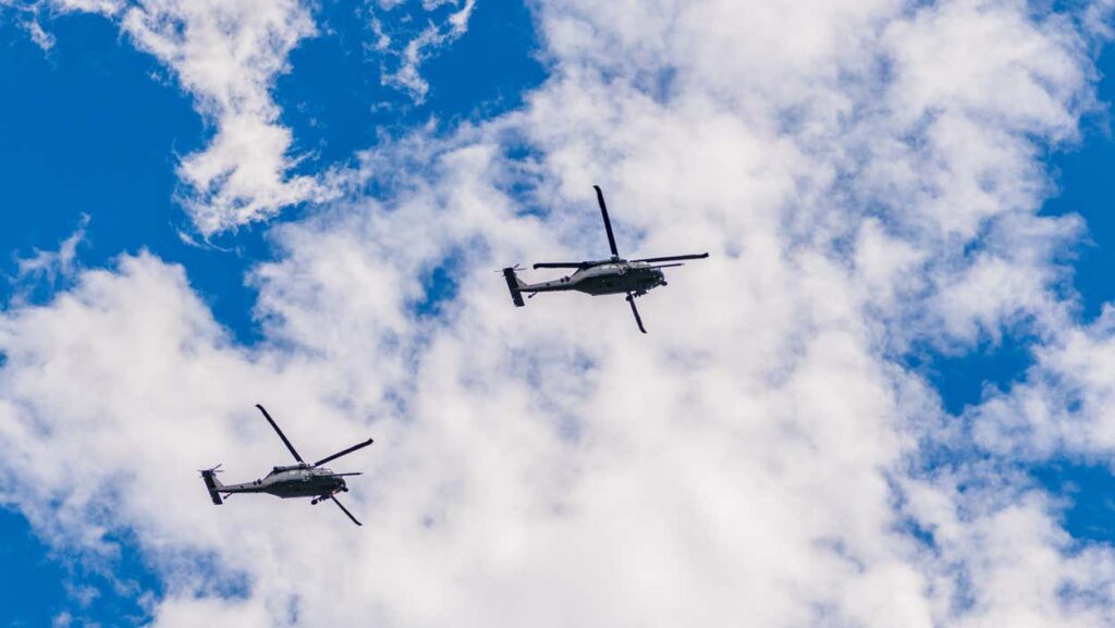 Dois helicópteros voando em formação contra um fundo de céu azul parcialmente nublado. Imagem para ilustrar post sobre pontos turísticos de São Paulo.