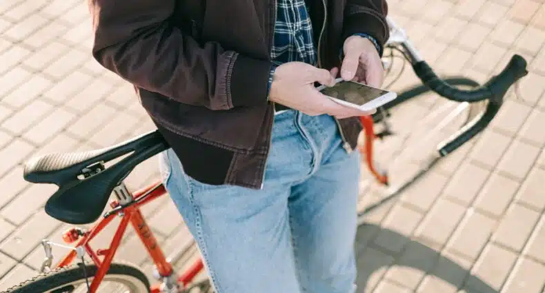 Uma pessoa de jeans e jaqueta está ao lado de uma bicicleta vermelha, usando um smartphone em uma superfície pavimentada. A imagem ilustra o post sobre eSIM internacional.