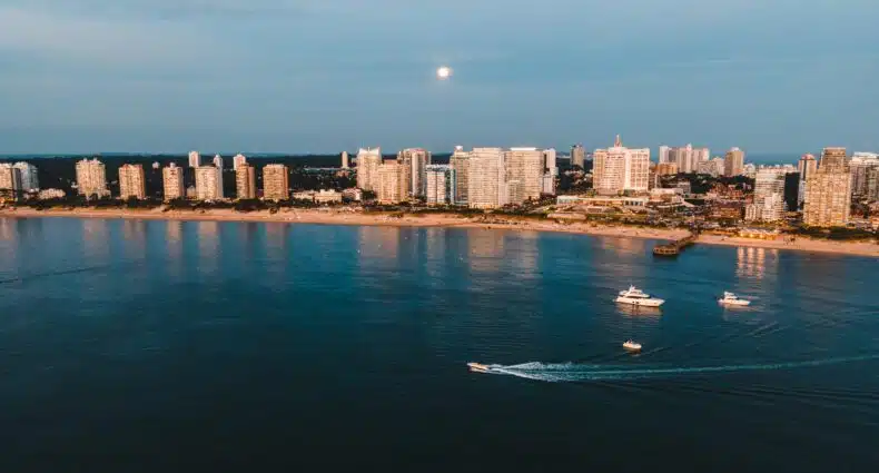 Vista aérea do horizonte de Punta del Este ao longo da costa, com barcos se movendo na água e edifícios refletindo a luz do entardecer. A foto ilustra o post de eSIM Uruguai.