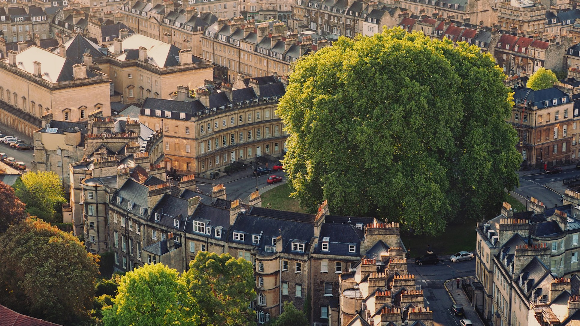 Vista aérea do The Circus, com fileiras de edifícios de pedra e uma grande e exuberante árvore verde no centro de uma praça. Foto para ilustrar o post de o que fazer em Bath.