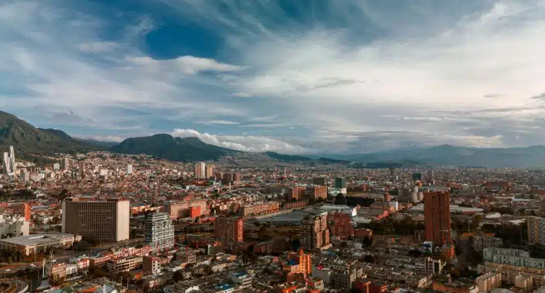 Uma vista ampla de uma cidade com muitos edifícios, cercada por montanhas sob um céu parcialmente nublado. A imagem ilustra o post sobre eSIM Bogotá.