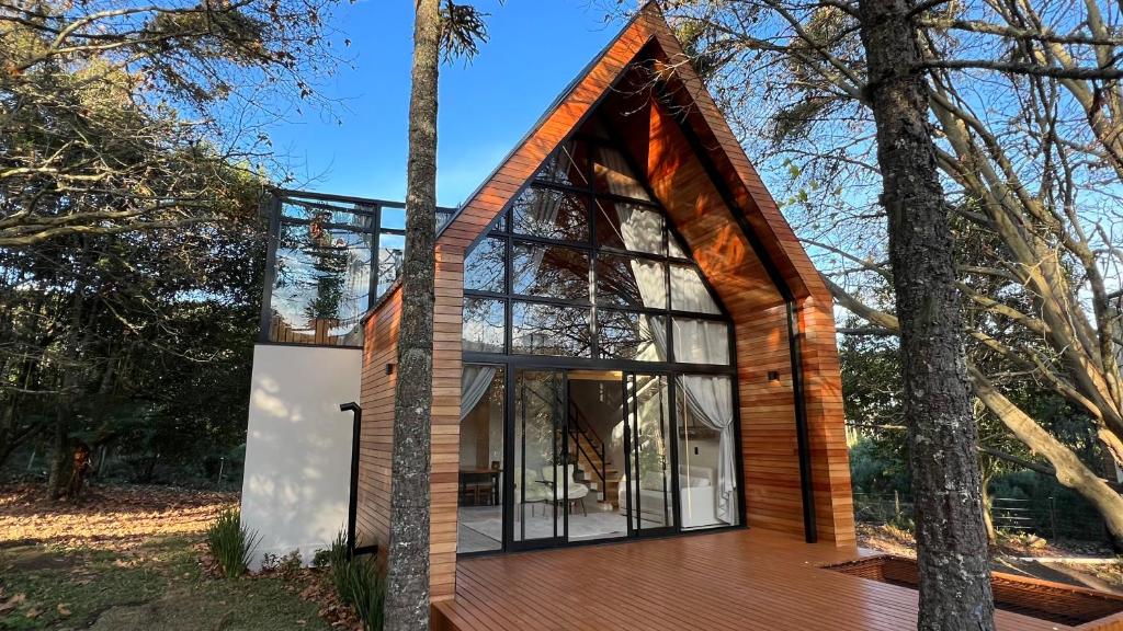Uma casa moderna em formato de A com grandes janelas de vidro e exterior de madeira, cercada por árvores e um deck de madeira.
