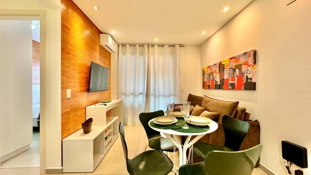 Uma pequena sala de estar e jantar com um sofá marrom, mesa redonda com quatro cadeiras, TV na parede e obras de arte abstratas, em uma das acomodações do Sky Batel - Apartamentos UROOMS.