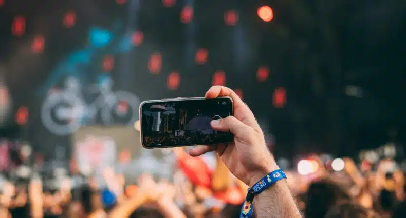 Uma pessoa segura um smartphone para gravar um show, com a multidão e o palco desfocados ao fundo. Ilustra o eSIM Hungria.