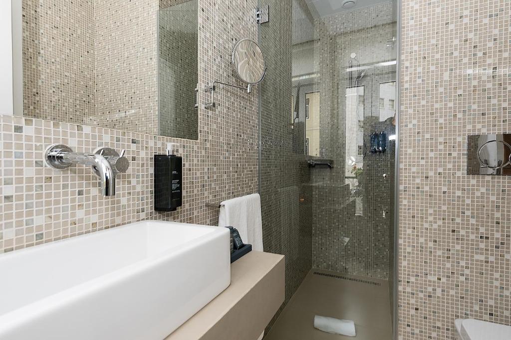 Banheiro moderno com paredes de mosaico, pia retangular, torneira de parede e chuveiro com box de vidro, em um dos quartos do The Leaf Boutique Hotel Lisbon.