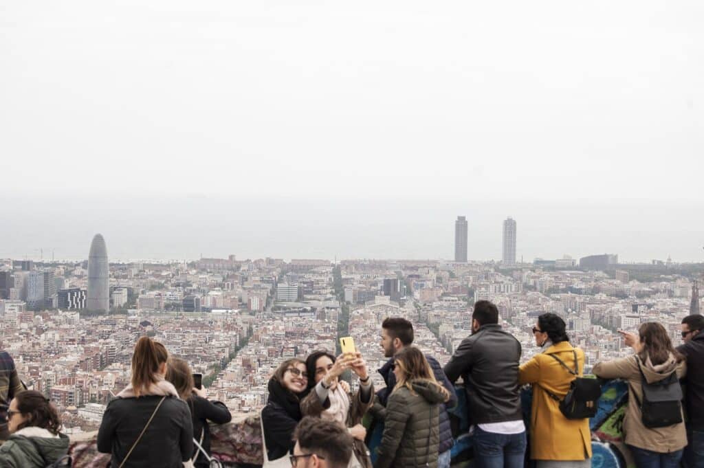 Um grupo de pessoas em um mirante tirando fotos, com uma paisagem urbana e o mar visíveis ao fundo. Ilustra o post sobre eSIM Barcelona.