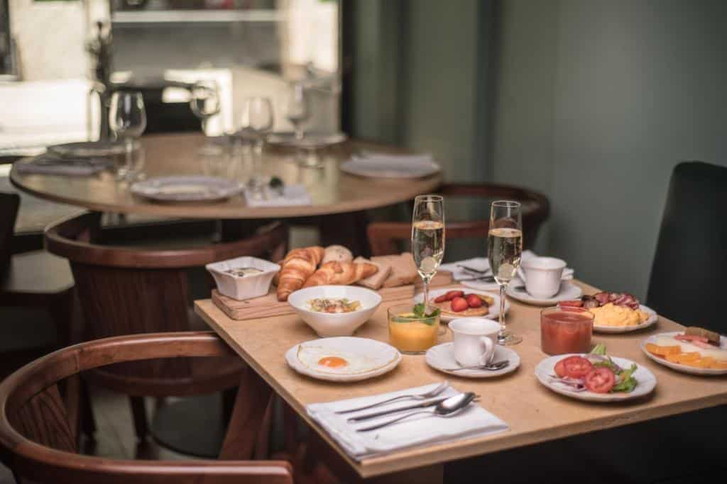 Uma mesa posta para o café da manhã com ovos, frutas, doces, suco, café e duas taças de vinho espumante, servido no Hotel da Baixa.