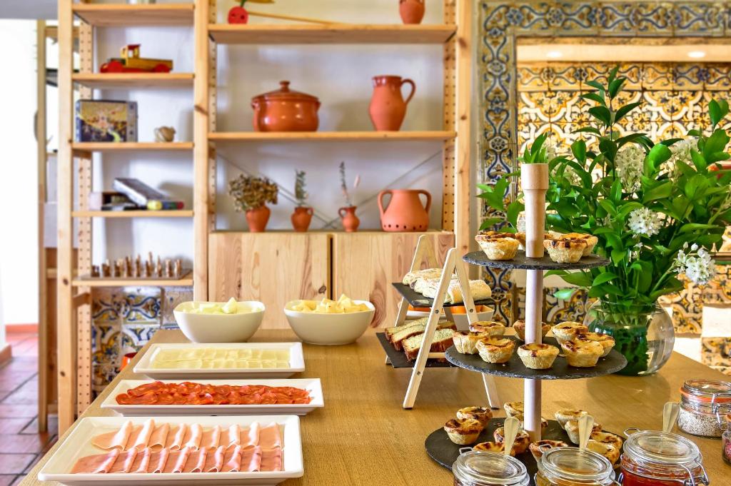 Um bufê de café da manhã com frios, queijos, doces, pães, potes de geleia e decoração em cerâmica ao fundo, servido no The Noble House – member of Unlock Hotels.