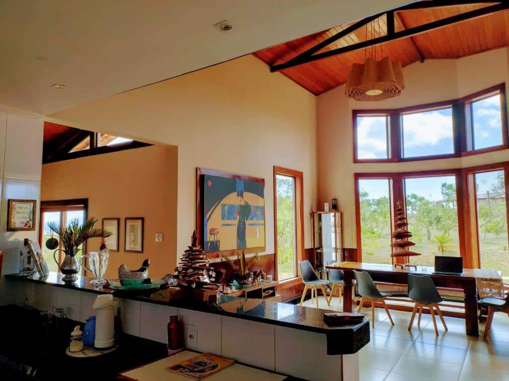 Moderna área de estar e jantar com grandes janelas, teto de madeira e móveis contemporâneos, com vista para a vegetação externa, na Casa Candeia.