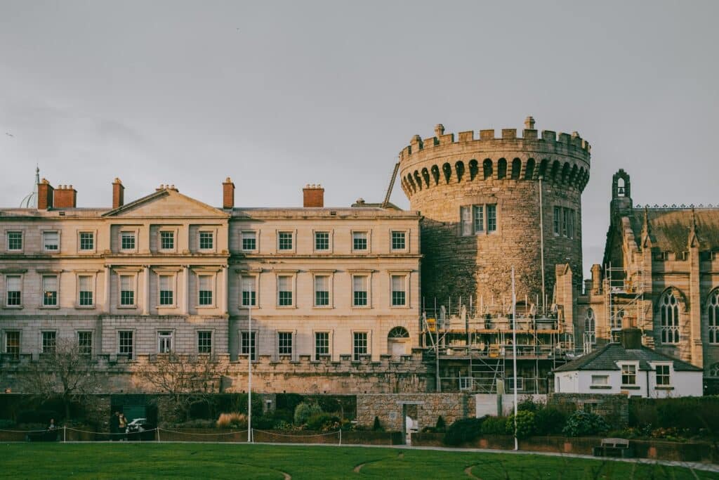 O histórico Castelo de Dublin de pedra com uma torre redonda e um edifício adjacente, cercado por grama e andaimes, que pode ser visitado com o eSIM Dublin.
