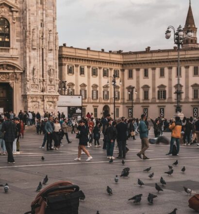 Pessoas se reúnem em uma grande praça da cidade com pombos no chão com a Catedral de Milão e outros edifícios históricos ao fundo, que pode ser visitada com o eSIM MIlão.