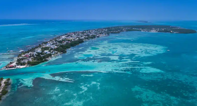 Vista aérea de Caye Caulker com águas azul-turquesa, áreas de areia branca e edifícios espalhados ao longo da costa. Imagem para ilustrar post sobre eSIM Belize.