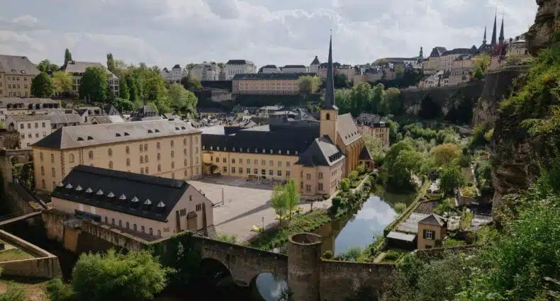 Uma vista da cidade de Luxemburgo com edifícios históricos, uma igreja com uma torre alta, uma ponte de pedra e um rio que pode ser visitada com o eSIM Luxemburgo.