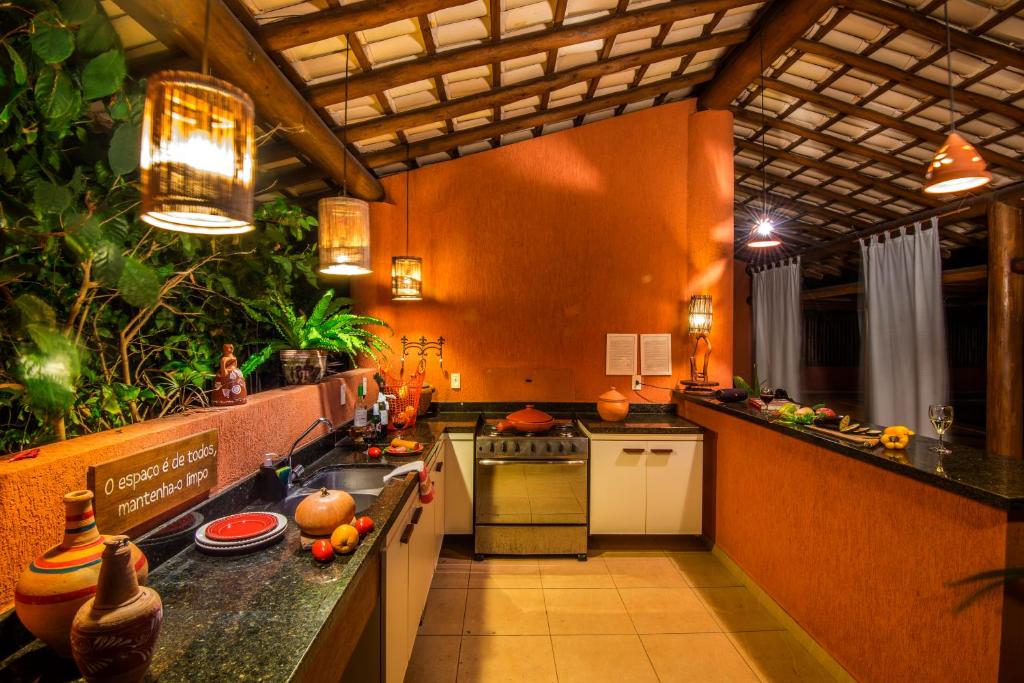 Cozinha externa com paredes alaranjadas, luzes penduradas, plantas e vários pratos e legumes nos balcões à noite, no Apartamento 2 quartos no Village Imbassaí Breeze, para representar airbnb em Imbassaí.