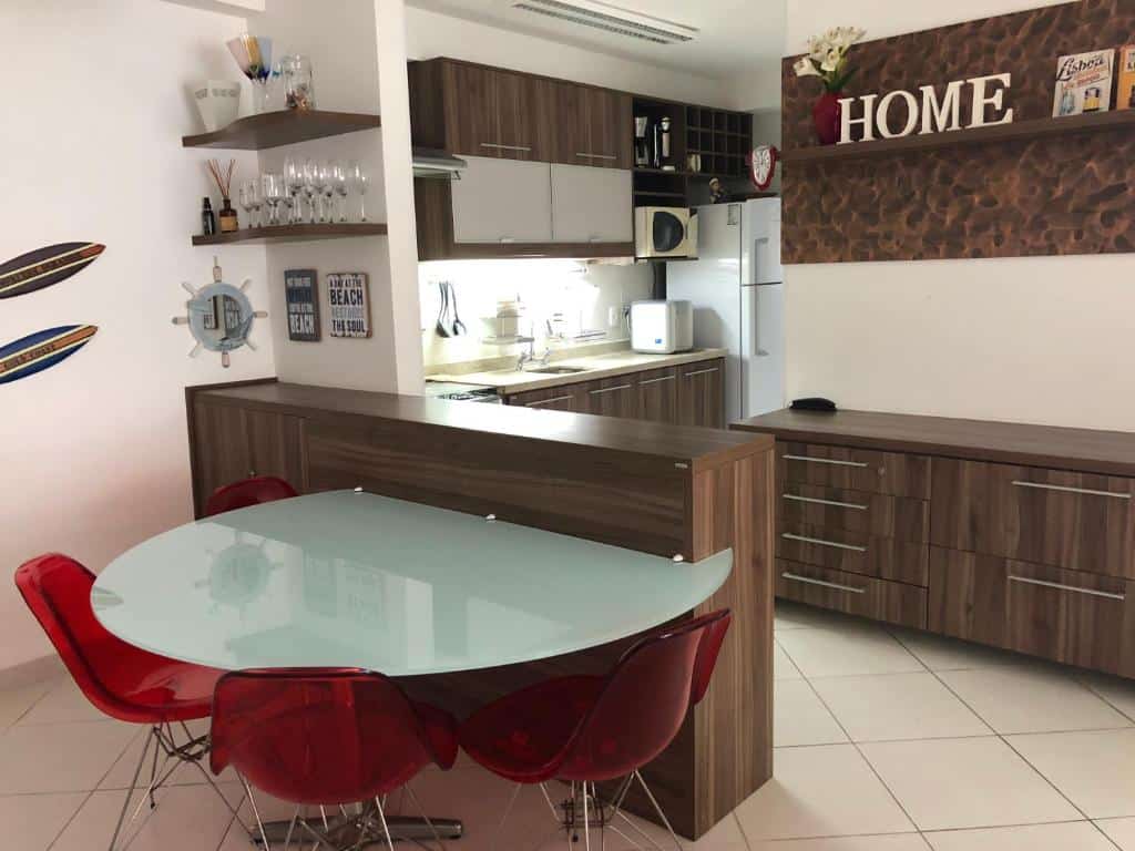 Cozinha moderna com armários de madeira, mesa de jantar de vidro, cadeiras vermelhas e uma placa decorativa "HOME" na parede, em uma unidade no Condomínio Reserva da Mata.
