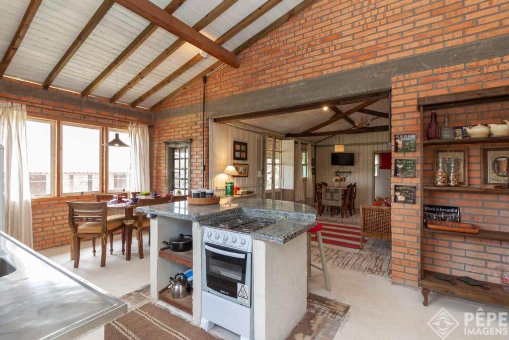 Cozinha aberta no Vieja Hacienda com paredes de tijolos, um fogão, área de jantar, prateleiras com decoração e vigas expostas no teto.