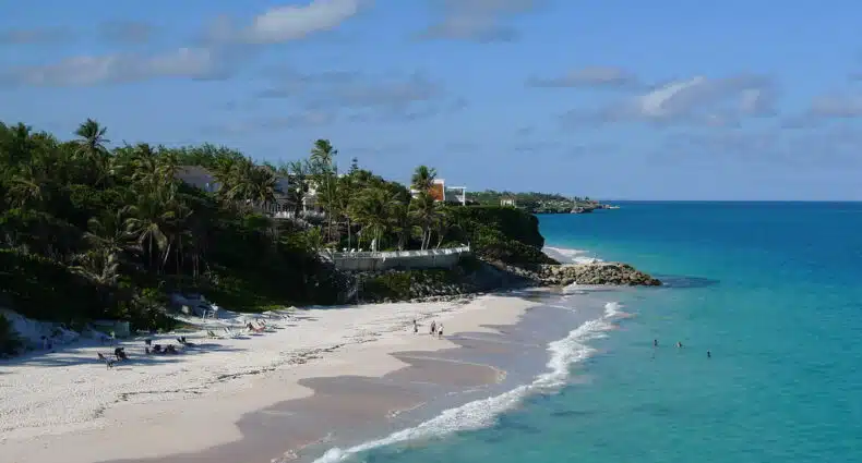 Crane Beach com águas azul-turquesa, pessoas nadando e palmeiras ao longo da costa sob um céu azul. Imagem para ilustrar post sobre eSIM Barbados.