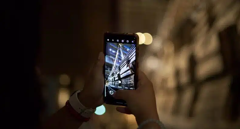 Uma pessoa segura um smartphone, tirando uma foto de um prédio alto e iluminado à noite, para ilustrar o post de eSIM Estocolmo.