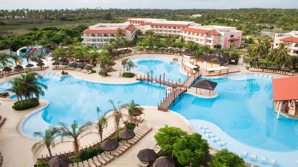 Um grande resort com várias piscinas, palmeiras, espreguiçadeiras, pontes e edifícios do hotel cercados por vegetação, trata-se do Grand Palladium Resort & SPA.