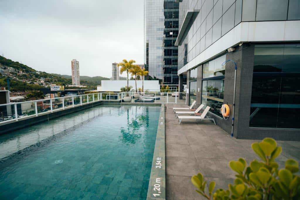 Piscina externa na cobertura ao lado de um edifício moderno com espreguiçadeiras, marcações na piscina e edifícios da cidade ao fundo, na propriedade do Hilton Garden Inn Itajaí - Praia Brava.