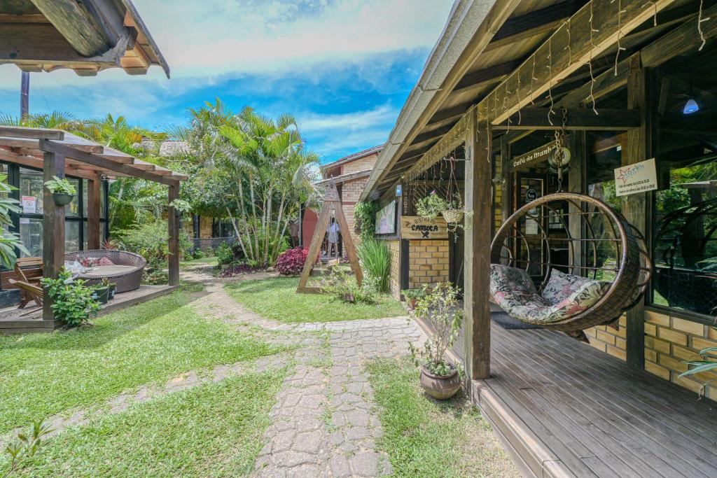 Jardim externo com caminhos de pedra, pátio de madeira, cadeira suspensa e pérgulas cercadas por vegetação sob um céu azul, na propriedade do Hotel Praia do Rosa.