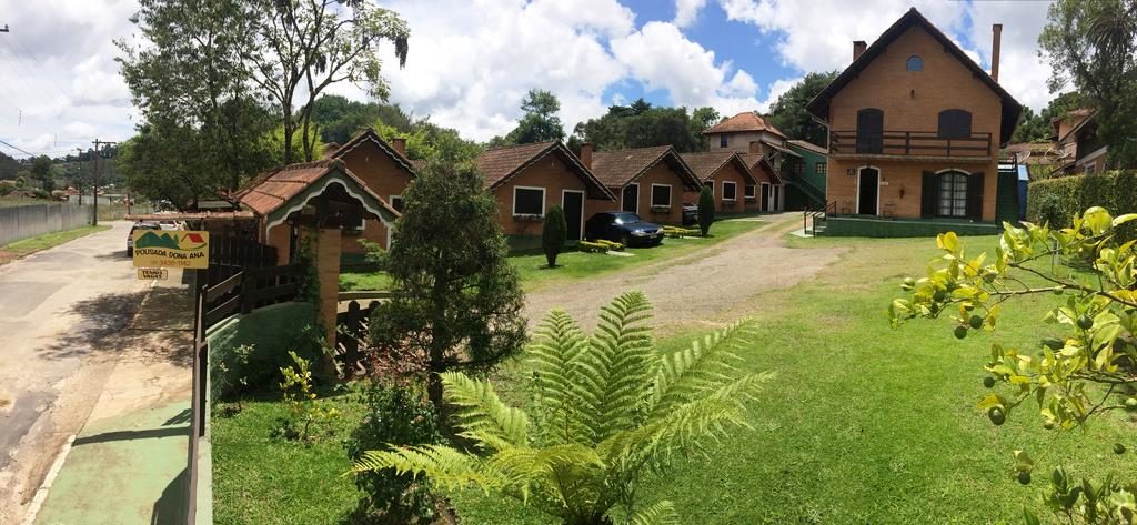Um grupo de casas de tijolos com gramados verdes, árvores e um carro estacionado perto do centro, na propriedade da Pousada Dona Ana.