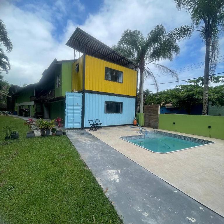 Um prédio de dois andares feito de contêineres de transporte ao lado de uma pequena piscina, cercado por grama e palmeiras, no Solaris do Una.