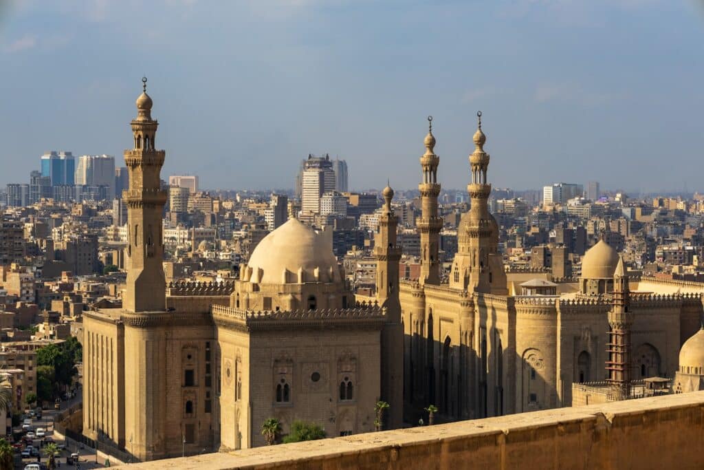 Uma vista da cidade com mesquitas históricas com grandes cúpulas e minaretes, cercadas por edifícios urbanos modernos, a Mesquita de Al-Rifa'i que pode ser visitada com o eSIM Cairo.
