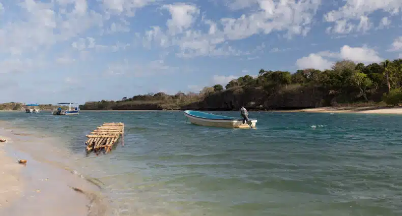 Três barcos, incluindo uma jangada de madeira, flutuam perto da Natadola Beach com um litoral arborizado e um céu parcialmente nublado. Imagem para ilustrar post sobre eSIM Fiji.