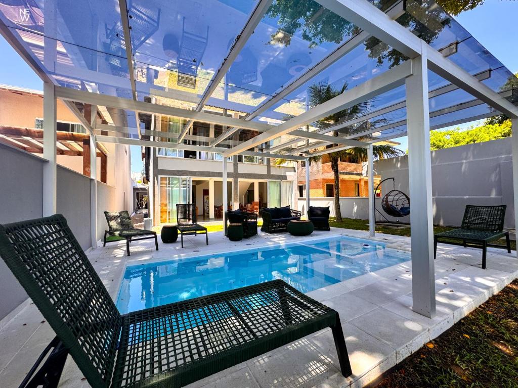 Piscina externa sob uma pérgola transparente com espreguiçadeiras, cercada por prédios e árvores em um pátio cercado, no OPY CAMBOA.