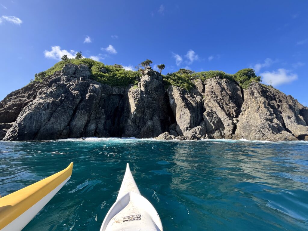 Duas canoas flutuam em águas azuis e cristalinas perto de penhascos rochosos com folhagem verde sob um céu azul brilhante.