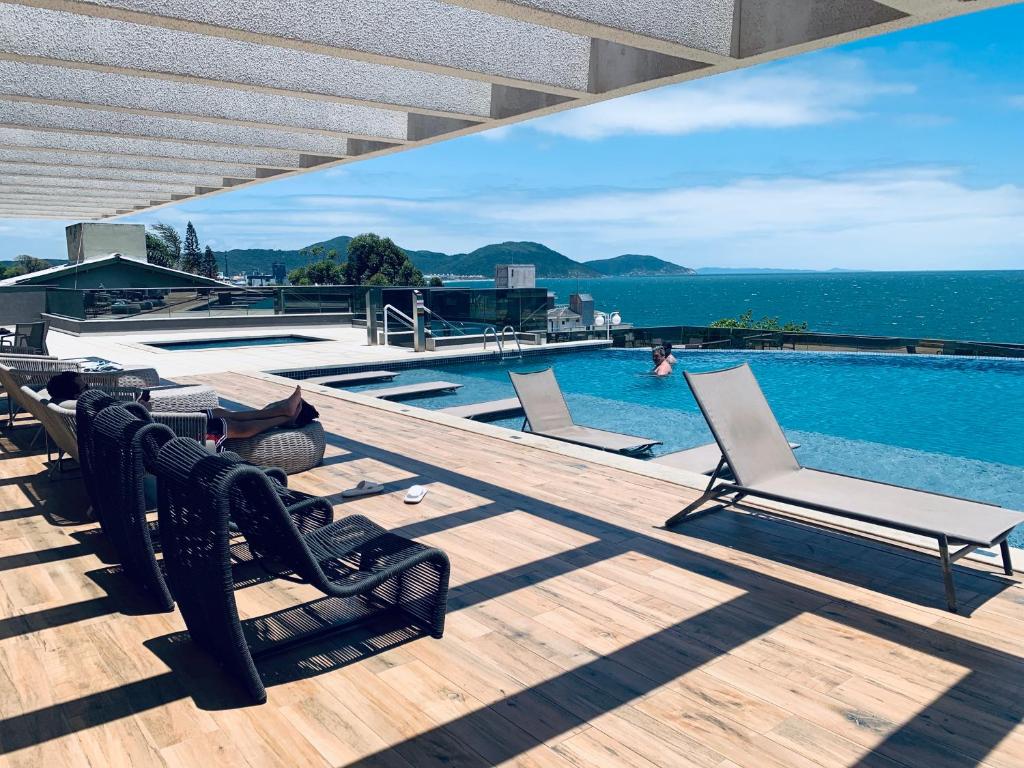 Área da piscina na cobertura com espreguiçadeiras, deck de madeira e vista para o mar sob uma pérgula parcialmente coberta, na Bela cobertura com vista para o mar.