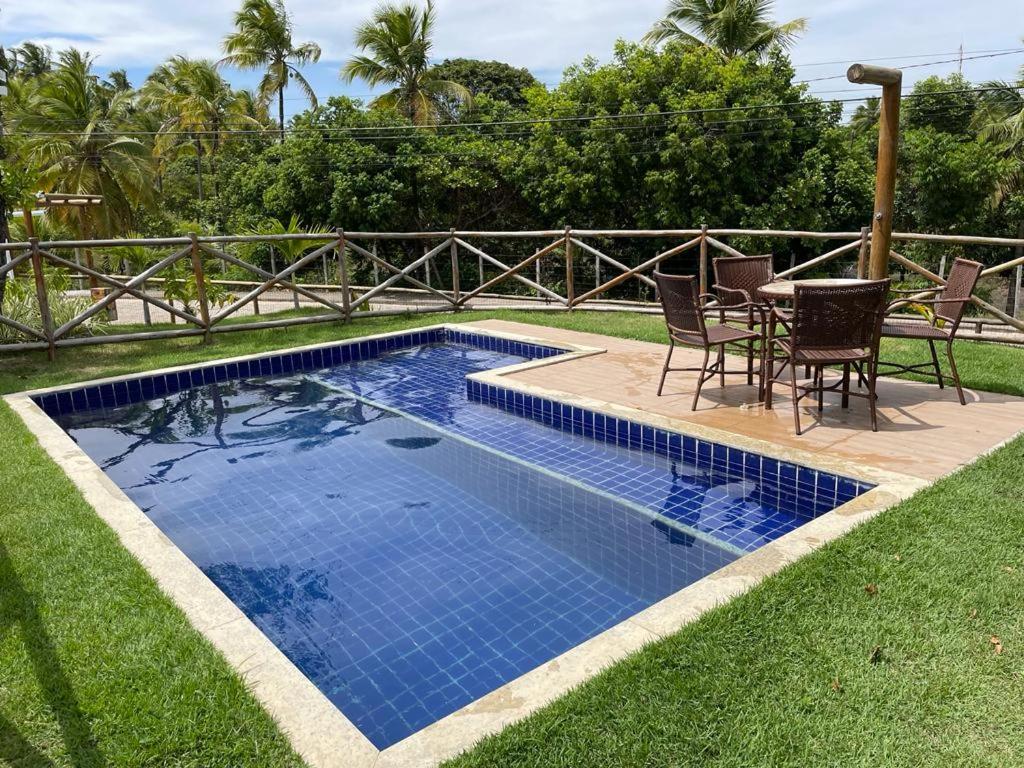 Pequena piscina retangular de azulejos azuis ao lado de um pátio com mesa, cadeiras e grama verde, cercada por uma cerca de madeira, na propriedade da Casa duplex de temporada.