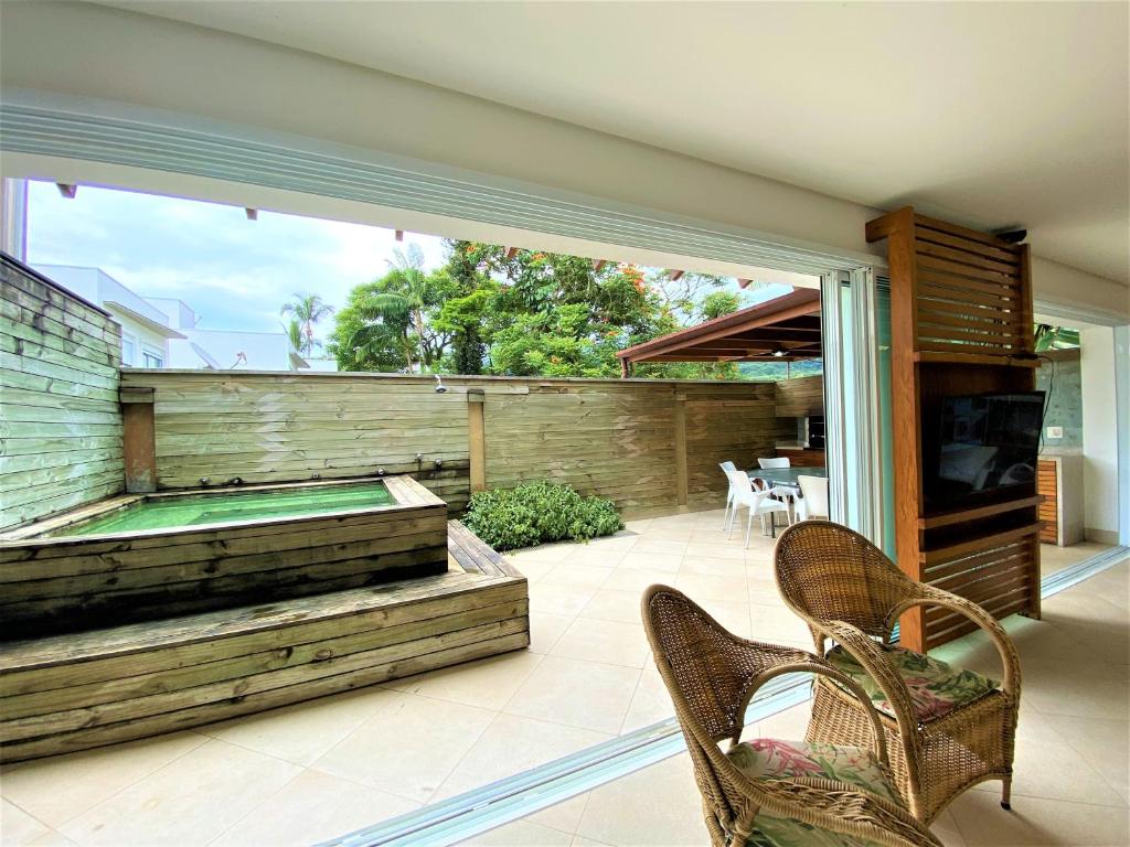 Pátio coberto com cadeiras de vime, banheira de hidromassagem de madeira, mesa de jantar e vegetação ao longo de uma área externa cercada, na propriedade da Casa na Praia maravilhosa de Juquehy.