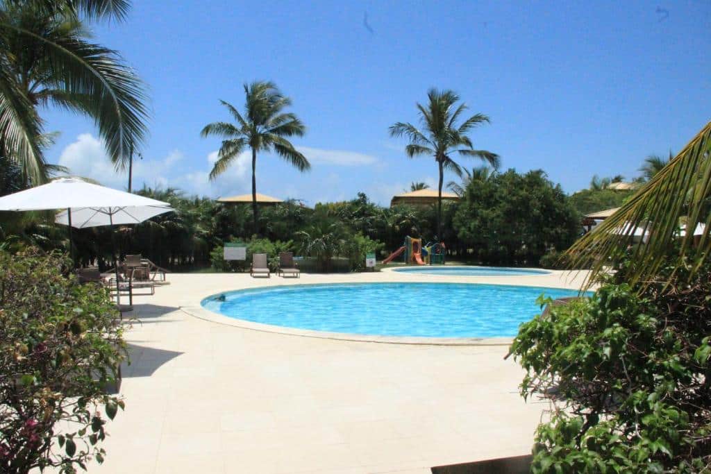 Uma piscina redonda ao ar livre cercada por espreguiçadeiras, palmeiras e vegetação sob um céu azul claro, na propriedade da Casa Peixinho.