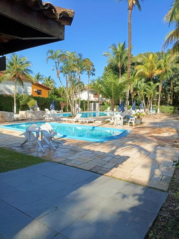 Área de piscina externa com espreguiçadeiras, palmeiras e um deck de azulejos sob um céu azul claro, na propriedade do Chalé Recanto do Barão.