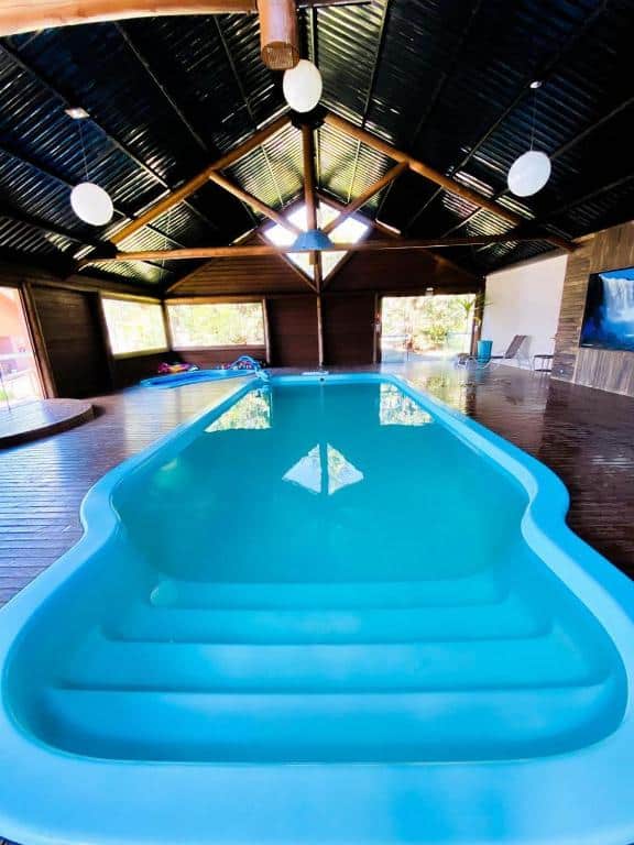 Piscina interna com água azul clara, deck de madeira, teto alto e janelas grandes que permitem a entrada de luz natural, no Eco Bouganville.