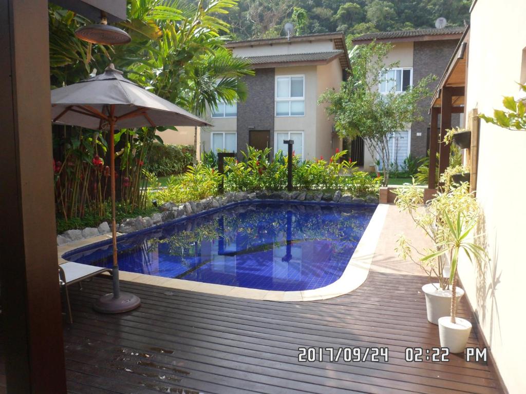 Uma pequena piscina externa com azulejos azuis é cercada por plantas e móveis de pátio entre duas casas modernas, na propriedade da Linda Casa em Juquehy,