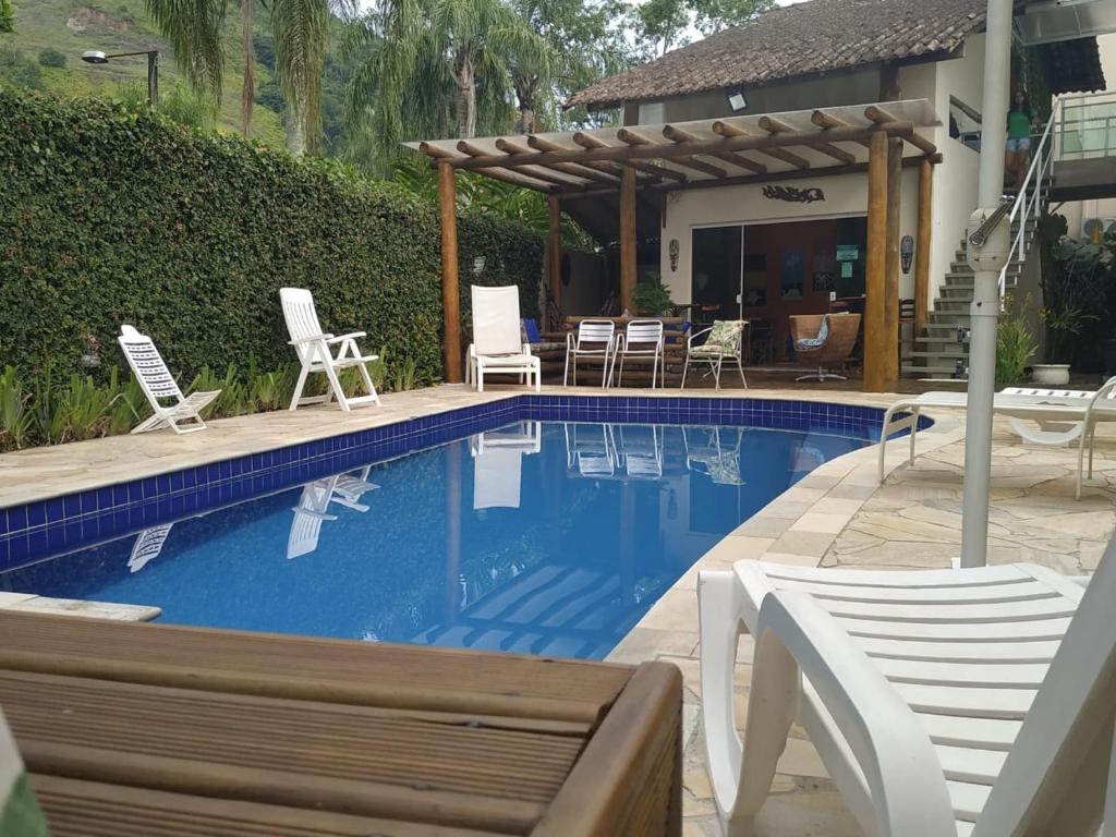 Piscina externa com água azul, cercada por espreguiçadeiras e um pátio, ao lado de uma casa com pérgola e escadas, na propriedade do Mares de Camburizinho.