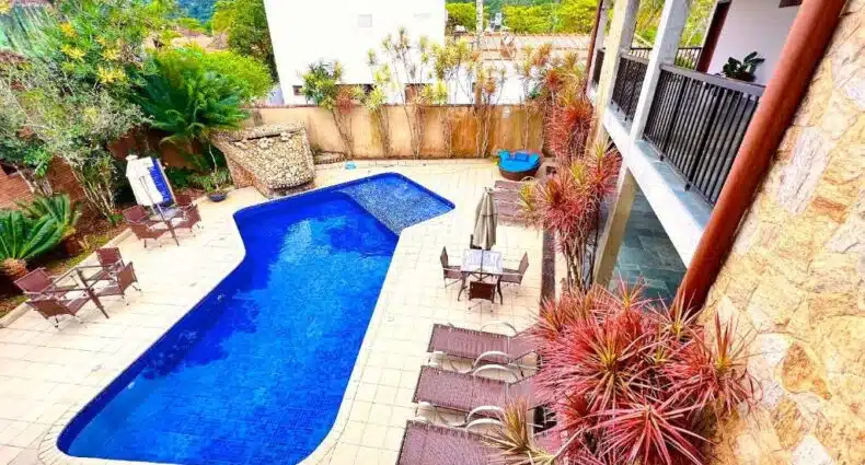 Piscina na propriedade da Pousada NAAN Lázaro Ubatuba vista de cima, com espreguiçadeiras ao redor e alguns vasos de flores, para representar pousadas na Praia do Lázaro em Ubatuba