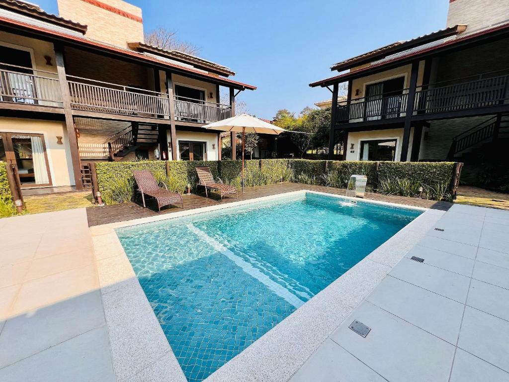 Piscina externa retangular com três espreguiçadeiras e guarda-sol, cercada por edifícios de dois andares e cercas-vivas, na propriedade da Pousada Rosa 08.