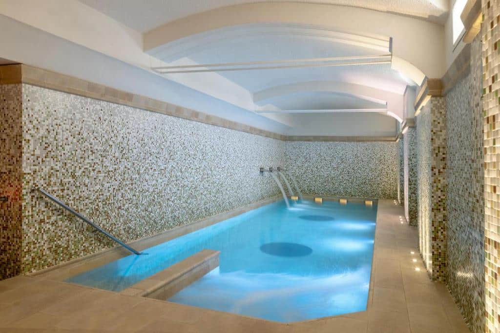 Piscina interna retangular com paredes de mosaico, degraus para a água e teto em arco com iluminação suave, na propriedade do UNAHOTELS Galles Milano.