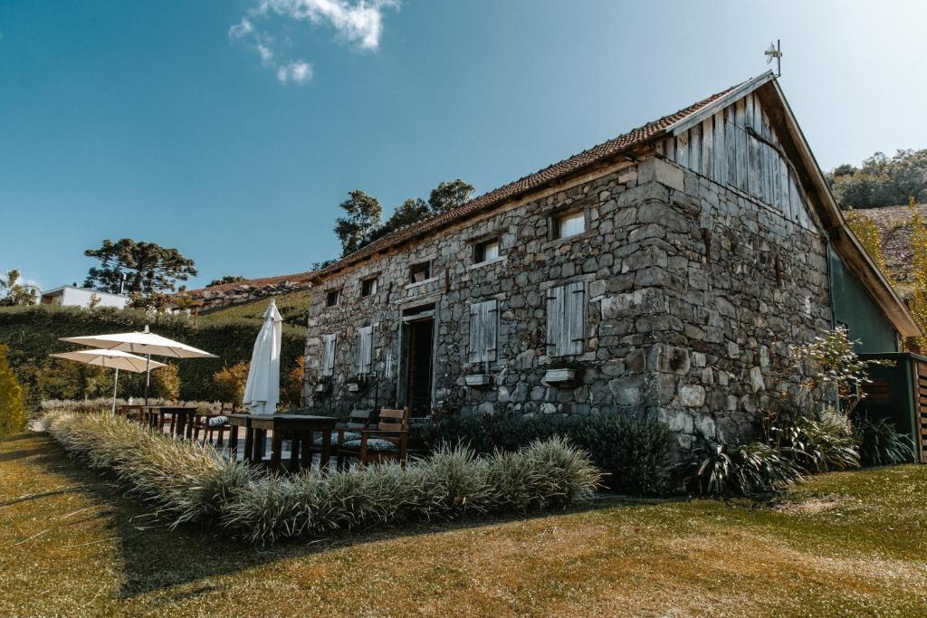 Uma casa de pedra com persianas de madeira fica ao lado de uma área de refeições ao ar livre com guarda-sóis em um gramado, trata-se da Pousada Cantelli em Bento Gonçalves.