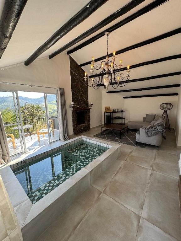 Uma moderna sala de estar com uma piscina de imersão interna de azulejos, lustre, área de estar, lareira e grandes janelas com vista para a montanha, em um dos quartos na Pousada Chalé da Montanha São Thomé das Letras.