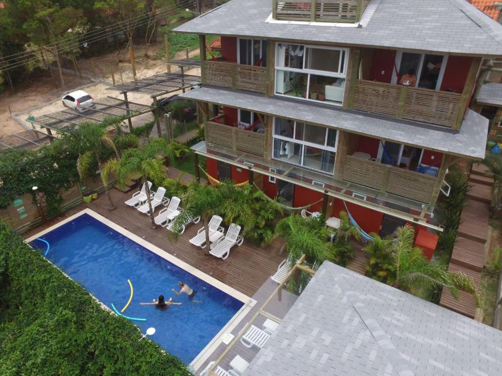Vista aérea de uma piscina, espreguiçadeiras, palmeiras e hóspedes nadando e relaxando ao ar livre, na propriedade da Pousada Morro do Rosa.