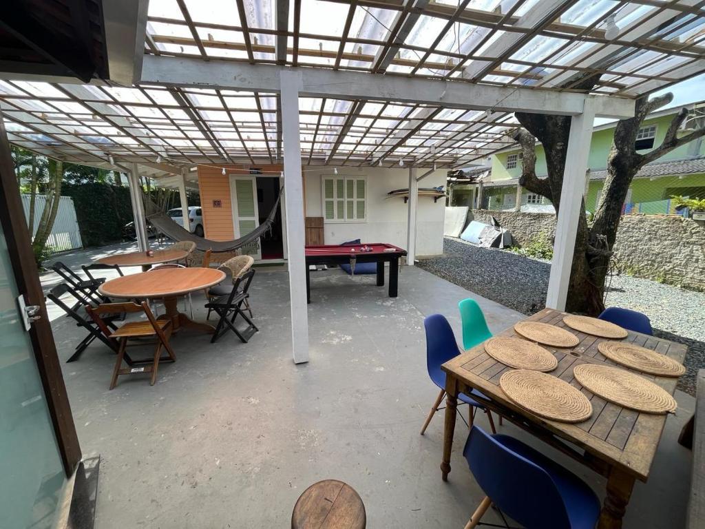 Pátio externo coberto com uma mesa de bilhar, rede, duas mesas de jantar, cadeiras e jogos americanos, ao lado de uma casa, na propriedade da Pousada Vale Beach.