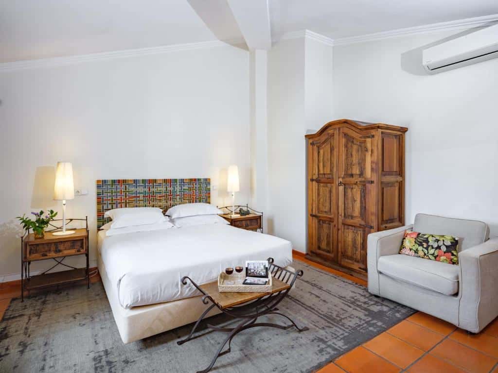Um quarto no ADC – Albergaria Do Calvário – member of Unlock Hotels com uma cama de casal, guarda-roupa de madeira, poltrona, mesas laterais com luminárias e uma pequena mesa de centro, para representar onde ficar em Évora.