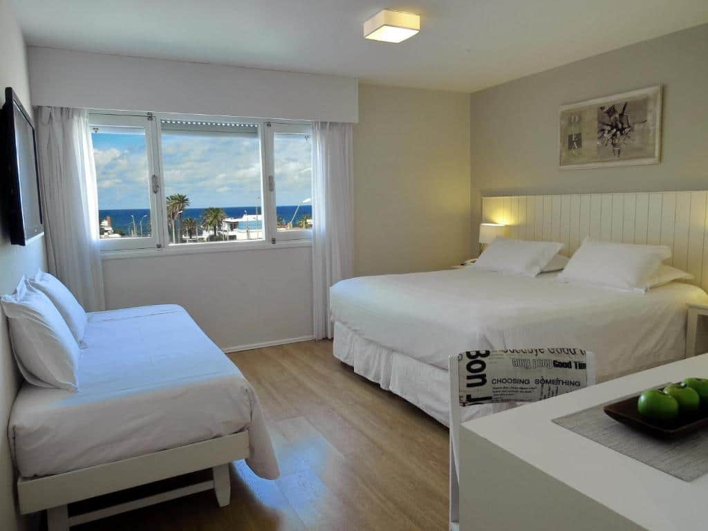 Um quarto no Atlántico Boutique Hotel com uma cama de casal, uma cama de solteiro, uma janela com vista para o mar, paredes brancas e piso de madeira.
