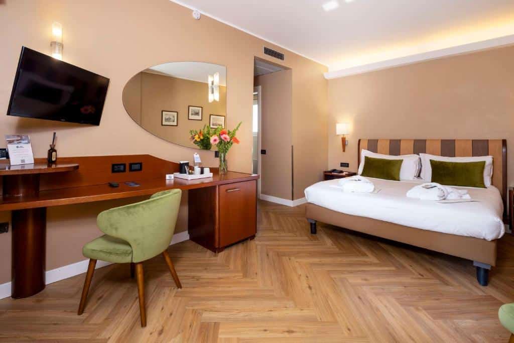 Quarto no Best Western Madison Hotel com uma cama de casal, escrivaninha, cadeira verde, TV na parede, espelho e piso de madeira, para representar hotéis Mercure em Milão.