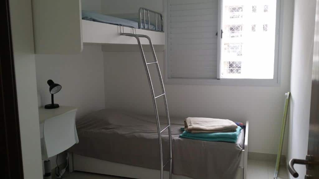 Um pequeno quarto com um beliche, uma escrivaninha com uma luminária e uma janela que permite a entrada de luz natural, no apartamento do Jd. S. Lourenço - Riviera, para representar airbnb na Riviera de São Lourenço.